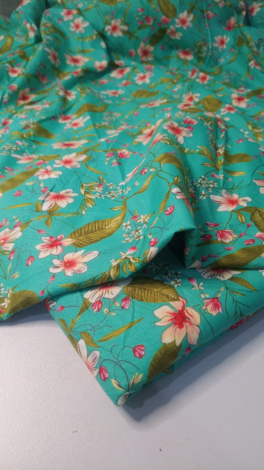 Floral fabric with pink flowers and green leaves on a turquoise background