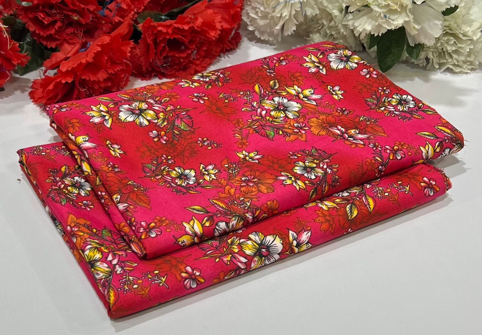 Folded fabric with floral pattern on a white surface with red and white flowers.