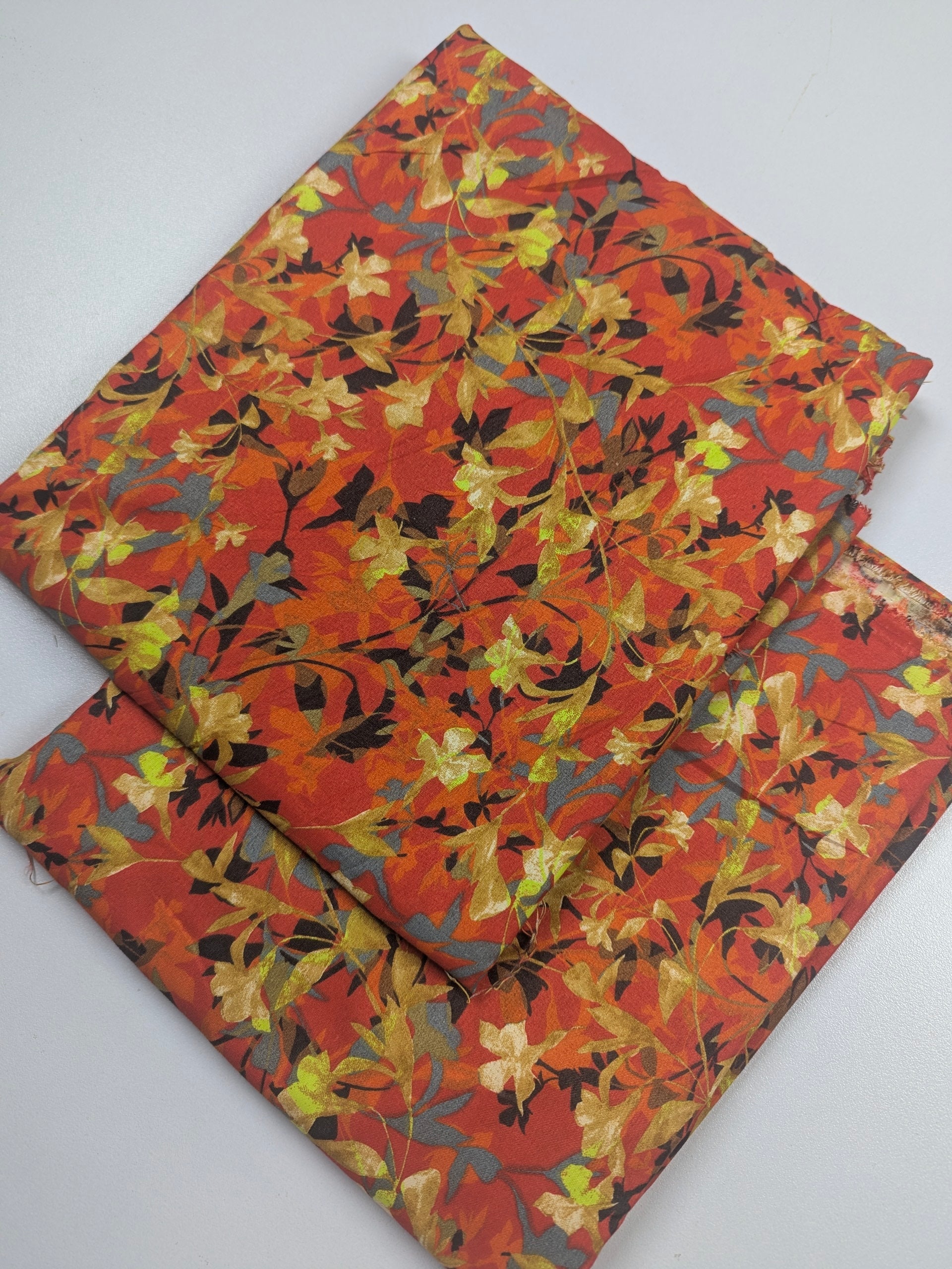 Two folded fabric swatches with a floral pattern on a white background