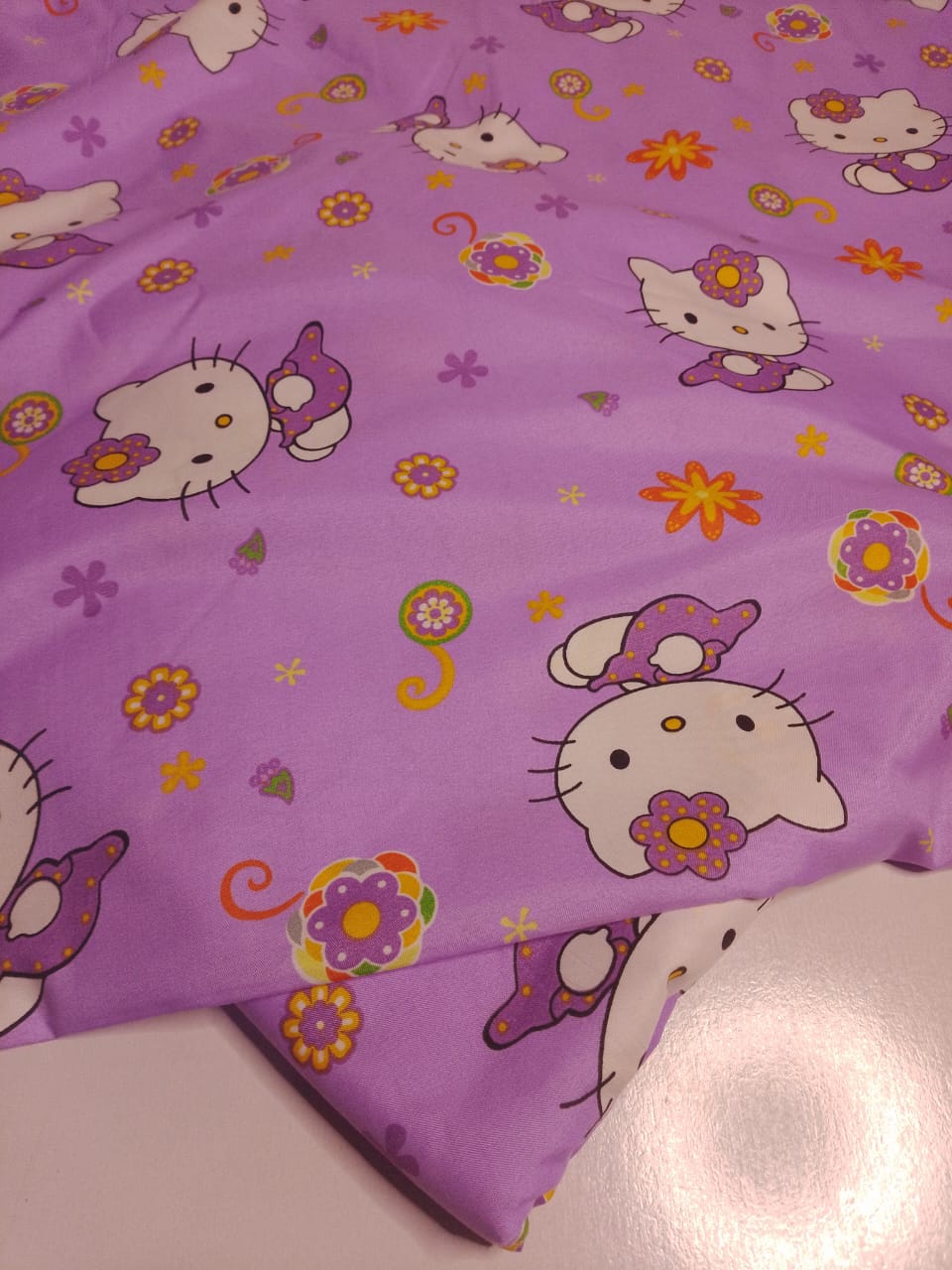 Purple fabric with cartoon cat designs and flowers on a white surface