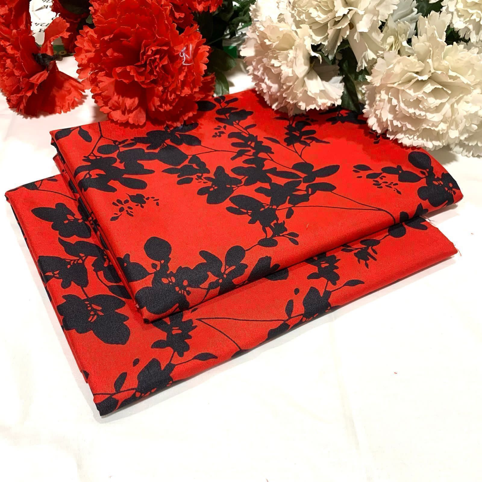 Red fabric with black floral pattern next to red and white flowers on a white background