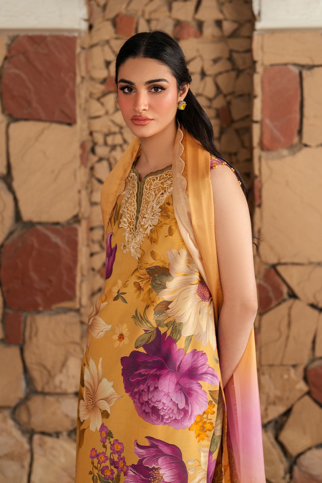 Woman wearing a yellow floral dress with a matching shawl against a stone wall.